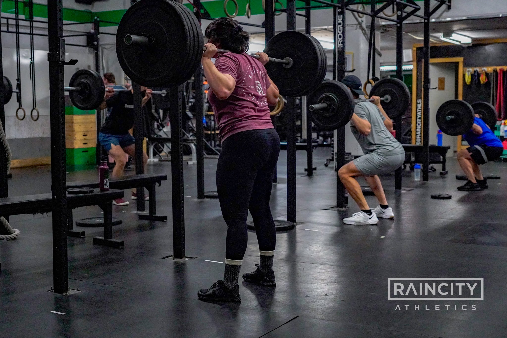 Athletes back squatting to build barbell strength in a Strength & Conditioning class
